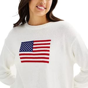 A woman is wearing a white sweater featuring a knitted American flag design on the front.