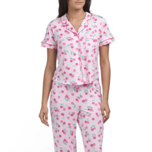 A woman is wearing pink pajamas with a cherry pattern, featuring a short-sleeved button-up top and long pants.