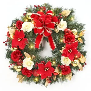 A festive wreath adorned with red and white flowers, gold balls, golden leaves, and a large red bow, accented by small lights and green foliage.