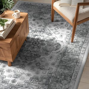 A room features a patterned rug with intricate designs, a wooden coffee table with books and a mug, and a cushioned chair with an open book.