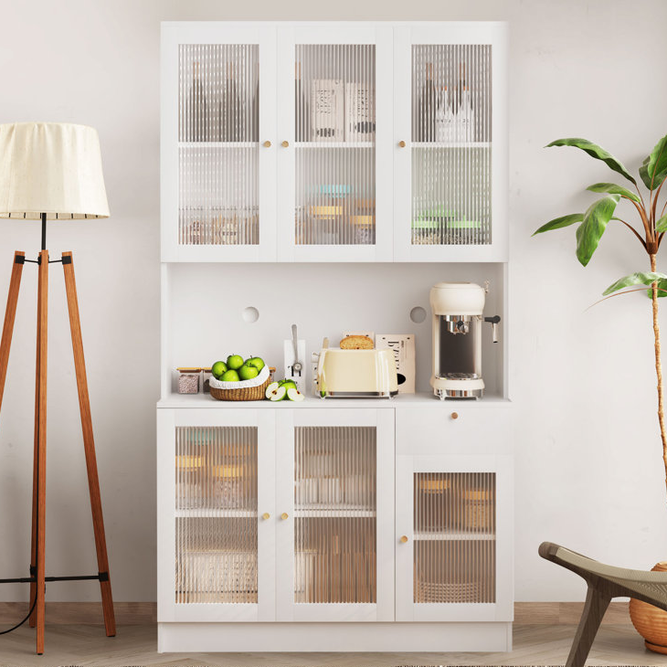 White storage cabinet with glass doors, a floor lamp, coffee maker, and a bowl of green apples.