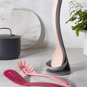 A set of nested pink and gray kitchen utensils on a countertop, with a cooking pot and a potted plant in the background.
