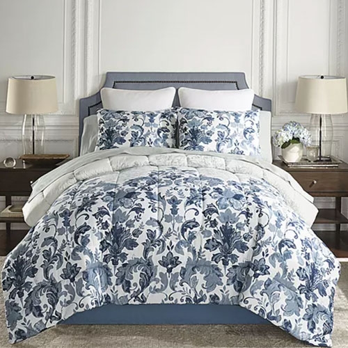 A bed with a blue and white floral-patterned comforter, matching pillows, and neutrally styled lamps on side tables.