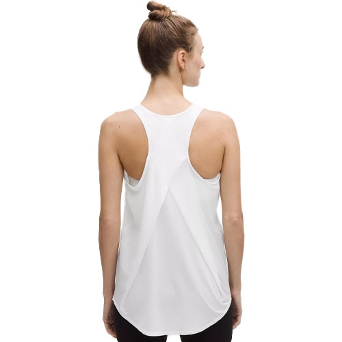 A woman wearing a white racerback tank top with a flowy design, paired with dark pants. The top features a rounded hem and is styled in a lightweight, breathable fabric suitable for casual or athletic wear.