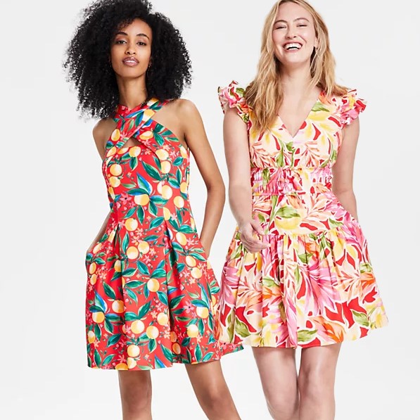 Two women wearing colorful floral dresses, one with a halter neck and the other with ruffled sleeves.