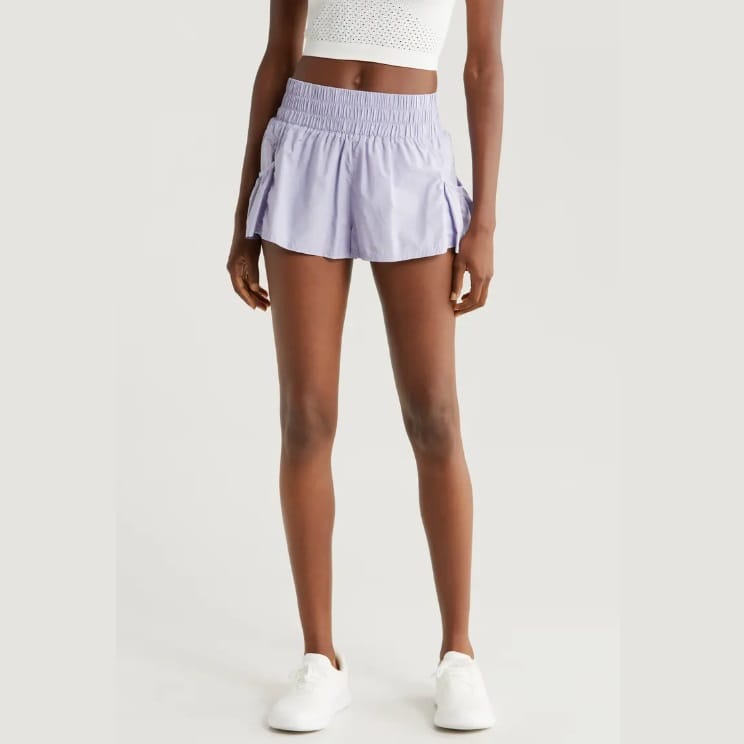 A person is wearing a white crop top, lavender athletic skirt, and white sneakers.