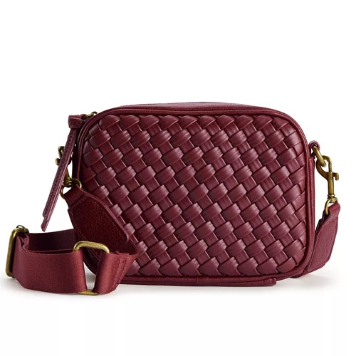 A compact maroon crossbody bag featuring a woven texture on the front, with an adjustable strap and gold hardware. The design is simple and elegant, suitable for carrying a camera or small personal items.