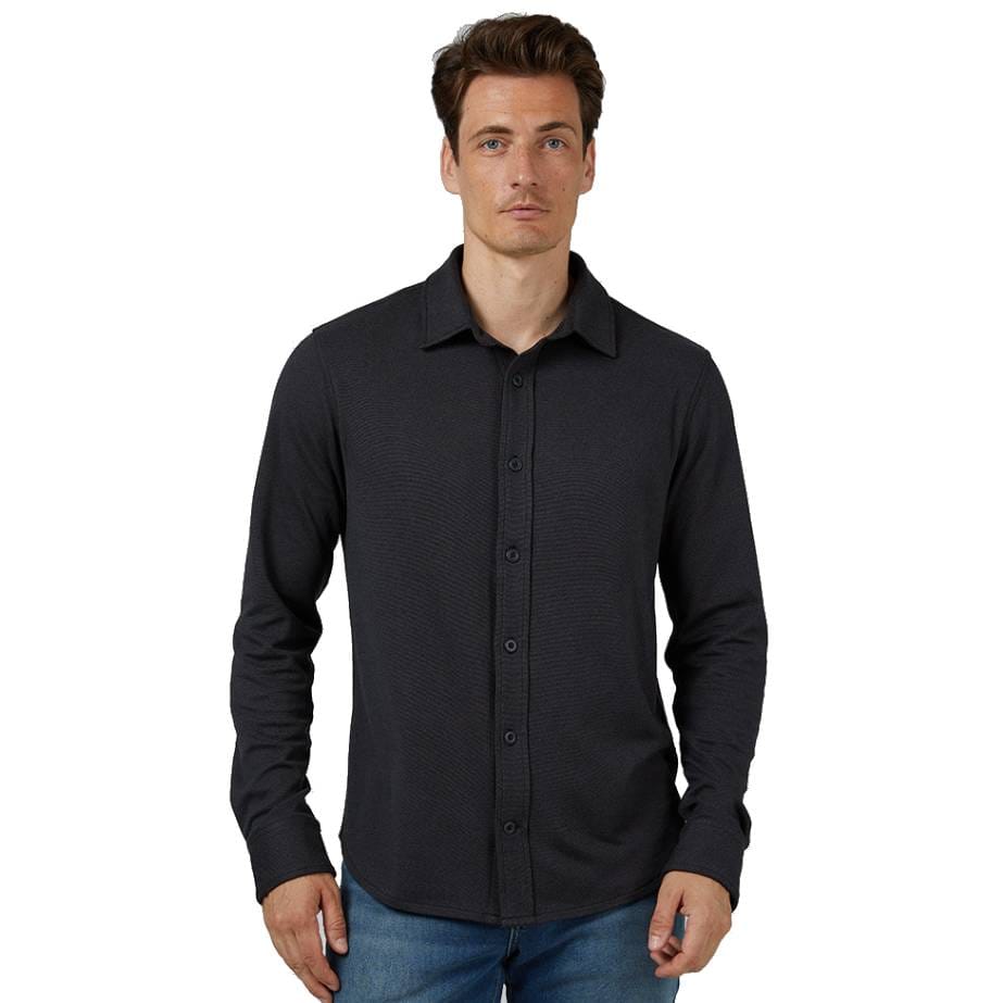 A man wears a long-sleeve, button-up, dark-colored Solid Stretch Shirt with a collar, paired with blue jeans.