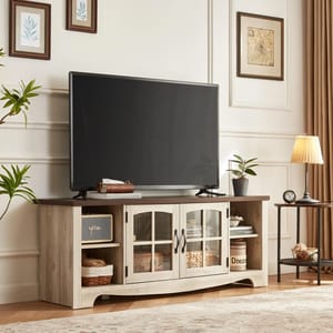 A flat-screen TV sits on a wooden TV stand with glass doors and decorative items, in a room with plants and framed art.