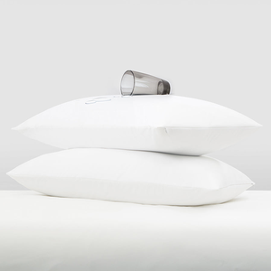 Two stacked white pillows with a clear glass of water resting on top.