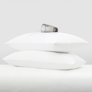 Two stacked white pillows with a clear glass of water resting on top.