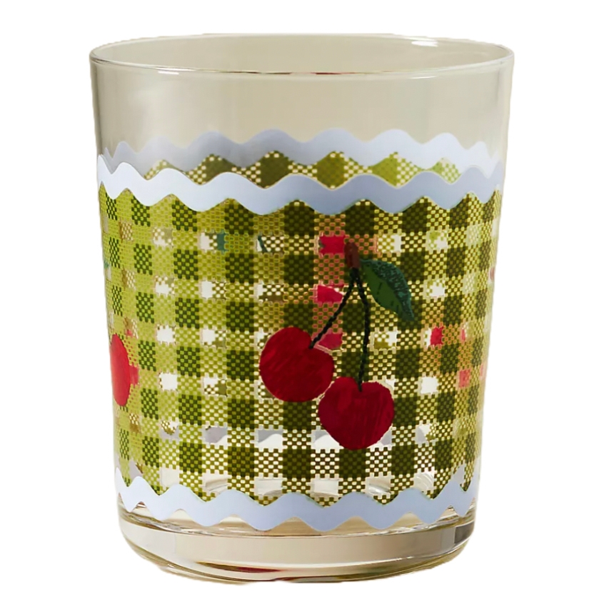 A drinking glass with a cherry motif against a green checkered pattern and bordered by a wavy white line.
