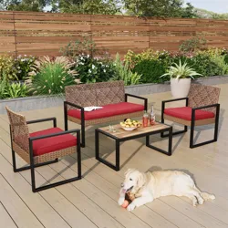 Outdoor patio set with red cushions includes a loveseat, two chairs, and a coffee table with a wooden top, placed on a wooden deck. A dog is lying on the deck.
