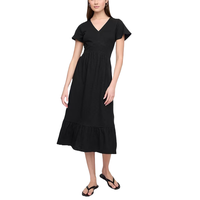 A woman is wearing a black midi dress with short sleeves, a V-neck, and a gathered waist. She pairs it with black flip-flops.