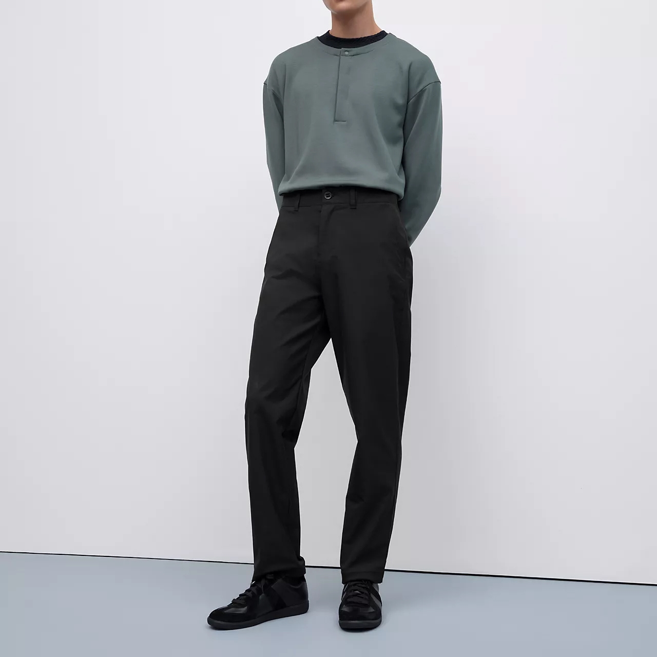 A person is wearing a green crew neck sweatshirt, black trousers, and black sneakers.
