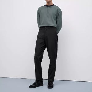 A person is wearing a green crew neck sweatshirt, black trousers, and black sneakers.