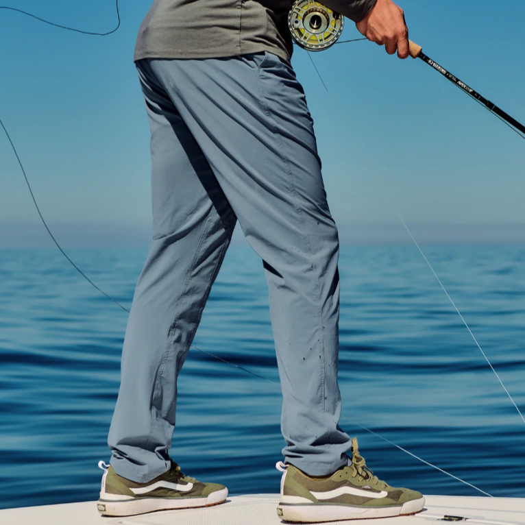 A person is on a boat holding a fishing rod, wearing a long-sleeve shirt, light blue pants, and green-and-white sneakers.
