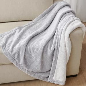 Gray and white reversible blanket with a leaf pattern, draped over a couch.