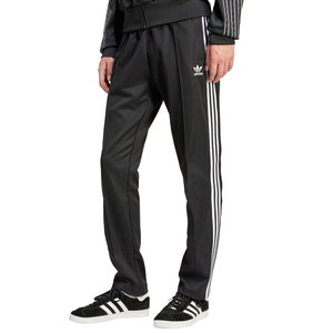 A person is wearing black Adidas track pants with white stripes and the brand logo, paired with black Adidas sneakers featuring white stripes.