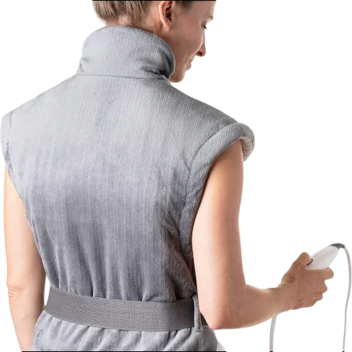 A person wearing a grey electric heating pad with a high collar, designed for neck and shoulder relief, holding a connected control device.