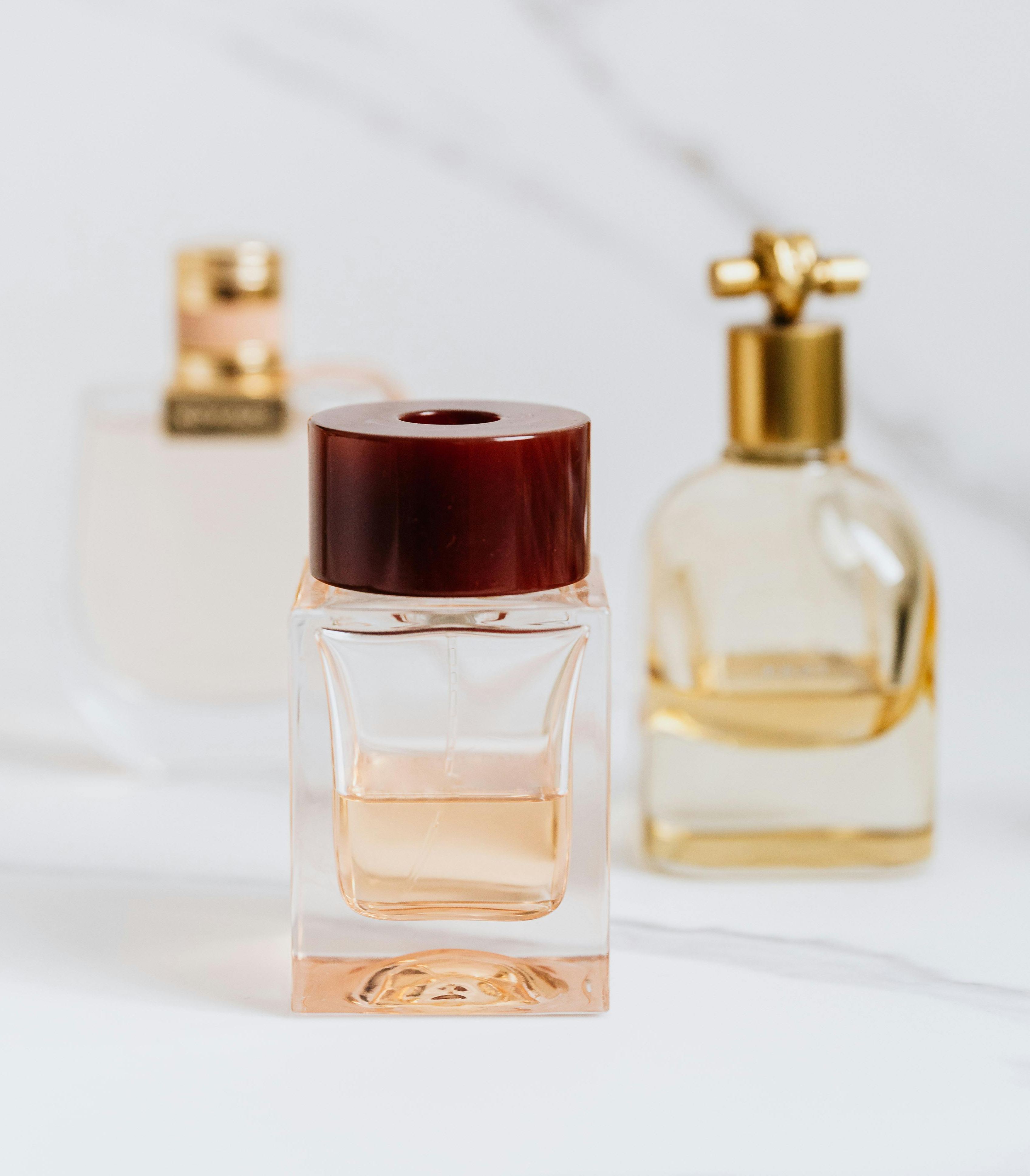 Three bottles of perfume with varying designs and colors, positioned on a marble surface.