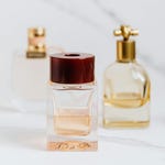 Three bottles of perfume with varying designs and colors, positioned on a marble surface.