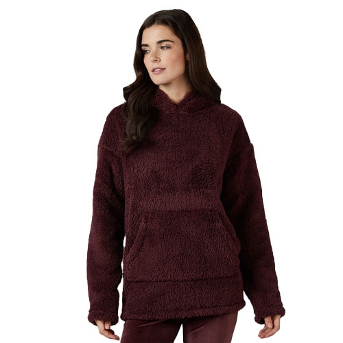 A woman is wearing a burgundy, plush sherpa hoodie with a front kangaroo pocket and relaxed fit.