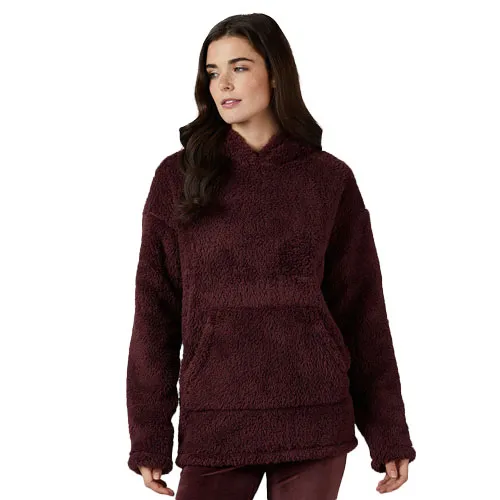 A woman is wearing a burgundy, plush sherpa hoodie with a front kangaroo pocket and relaxed fit.