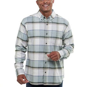 A man is wearing a button-up long-sleeve plaid shirt in tones of gray, white, and blue, featuring a front pocket and buttoned collar.