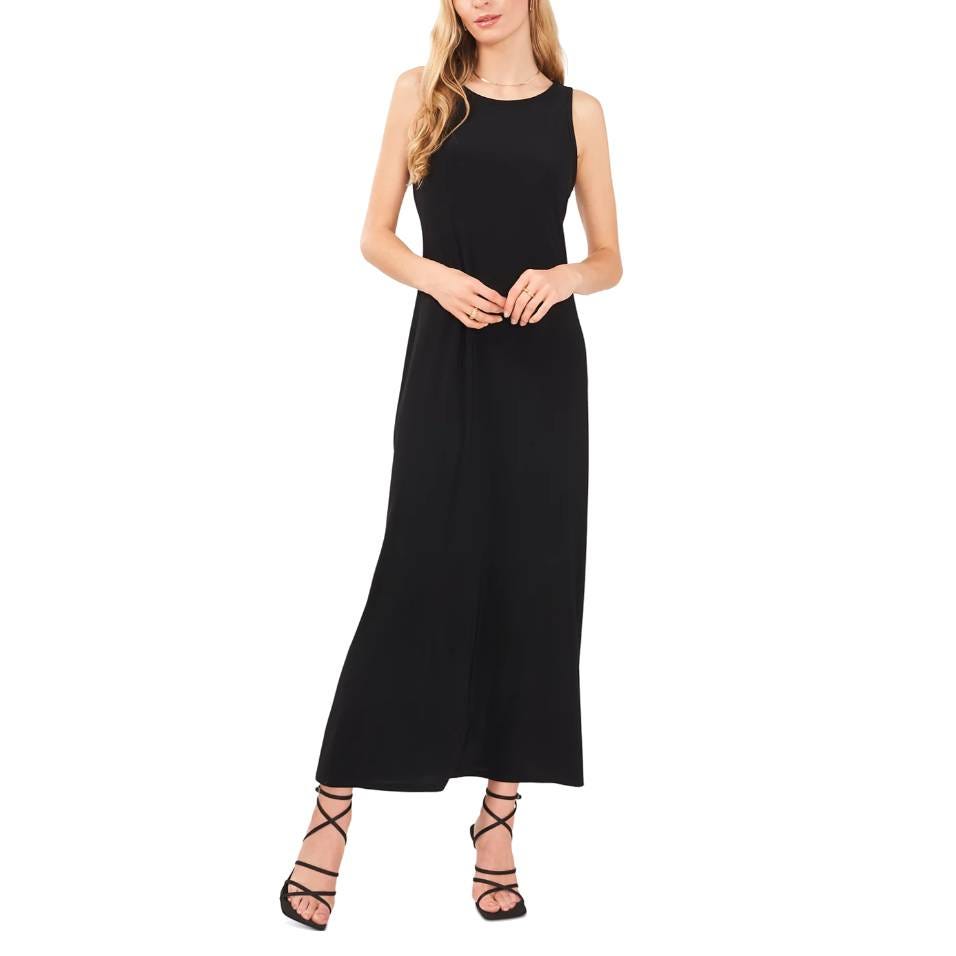 A woman is wearing a sleeveless black maxi dress with a keyhole neckline detail, complemented by strappy black sandals.