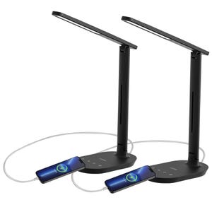Two black LED desk lamps with adjustable arms and built-in USB ports for charging devices are connected to smartphones via charging cables.