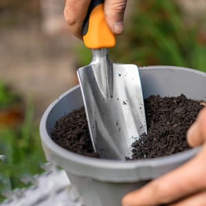 A gardening trowel with a bright orange and black handle and a sturdy metal blade, suitable for digging and transferring soil in gardening tasks.
