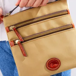 A tan Dooney & Bourke crossbody bag with two front zippered pockets, leather trim, and gold-tone hardware, featuring the brand's embossed logo on a circular leather patch.
