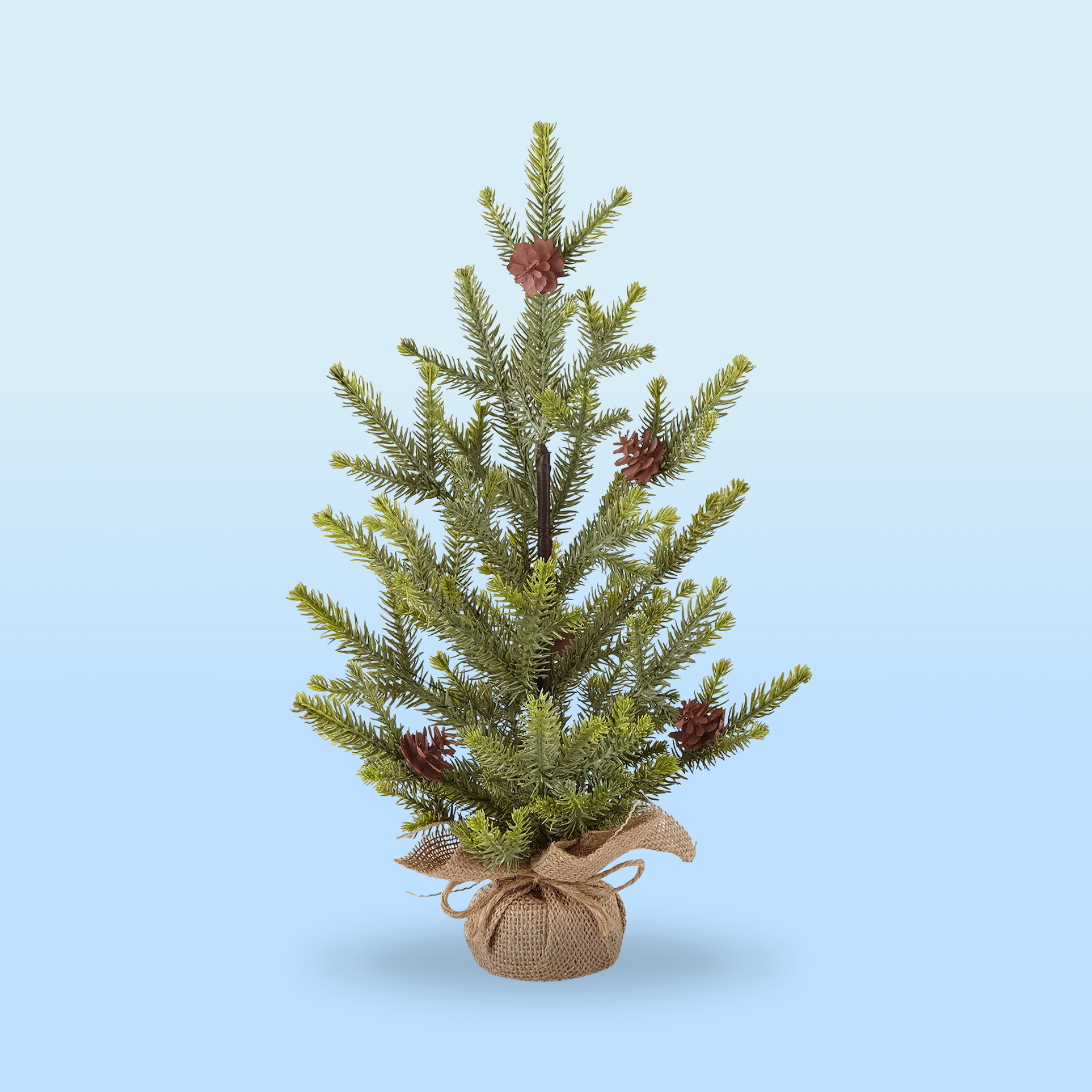 A small artificial Christmas tree with pinecones, set in a burlap-wrapped base, against a light blue gradient background.