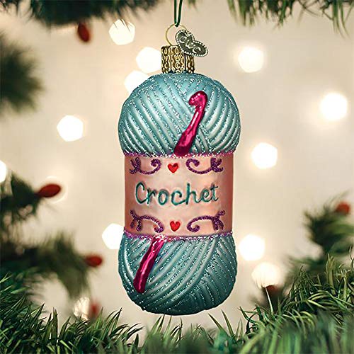 A Christmas ornament shaped like a skein of yarn, featuring the word \“Crochet\“ and small decorative hearts and scrolls, accented with a red crochet hook, hanging on a tree.