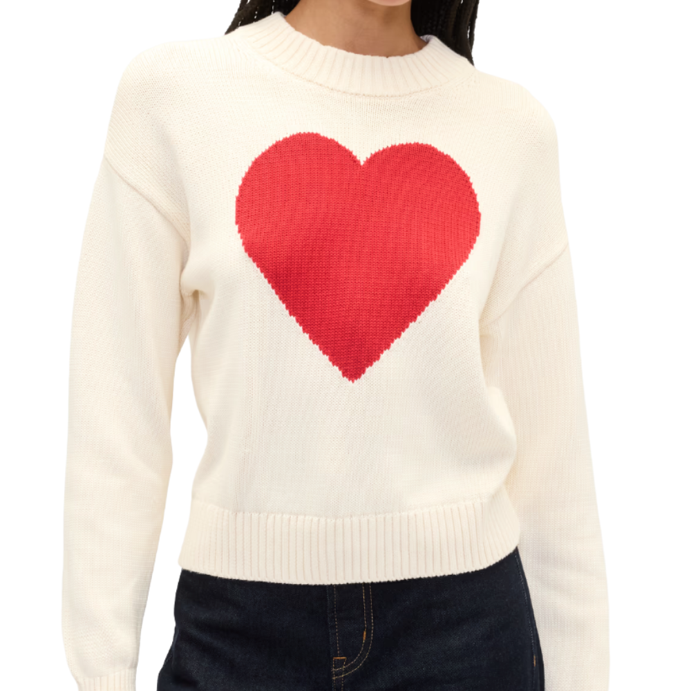 White sweater featuring a large red heart design on the front, worn by a person with dark jeans.