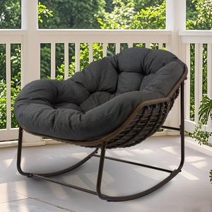 A cushioned papasan chair with a metal rocking frame is placed on a porch, surrounded by greenery.