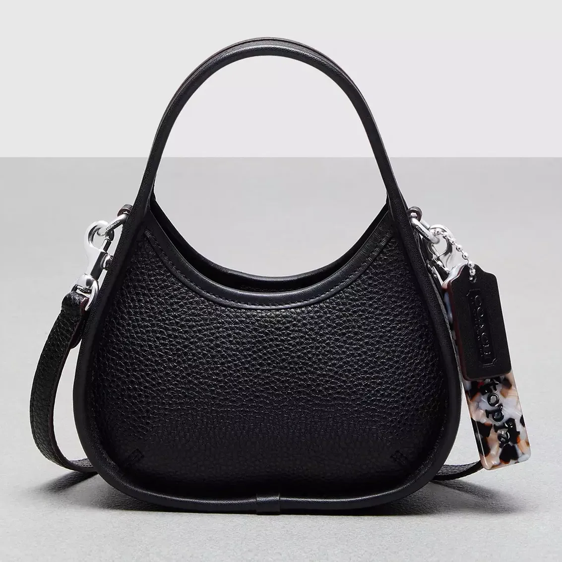 Black leather handbag with a curved top handle, detachable strap, and decorative tag.