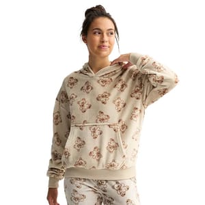A person models a cozy beige hoodie and matching pants featuring a teddy bear pattern.