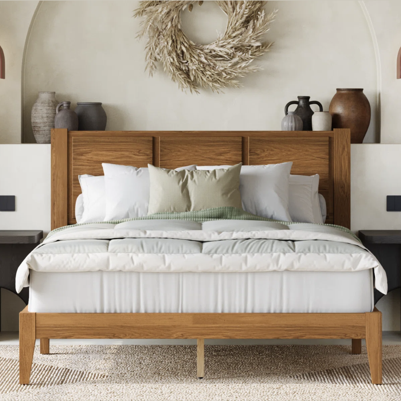 A wooden bed with a simple headboard is adorned with white and green bedding and pillows. A wall wreath and various vases decorate the headboard area, adding a rustic touch.