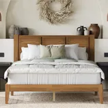 A wooden bed with a simple headboard is adorned with white and green bedding and pillows. A wall wreath and various vases decorate the headboard area, adding a rustic touch.