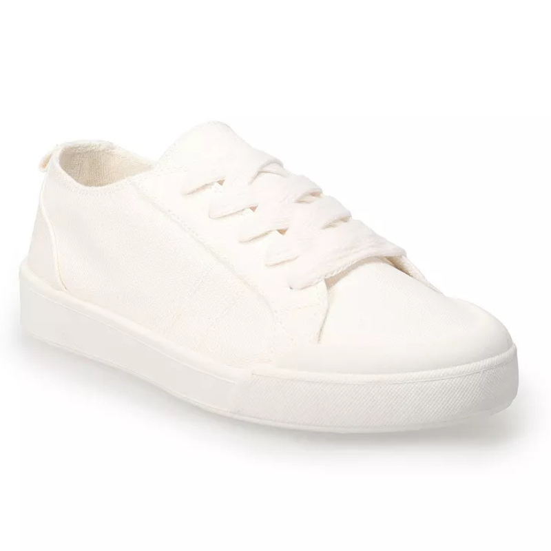 A white casual sneaker with a low-top design, featuring a canvas upper and white laces.