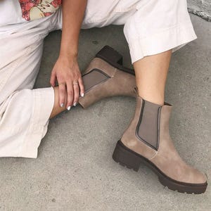 A pair of beige Chelsea boots with thick soles, paired with light-colored rolled-up trousers.