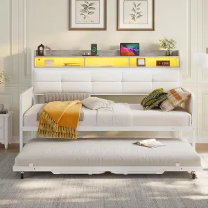 Modern trundle bed with a padded headboard featuring built-in shelving, ambient lighting, and electronic charging ports; decorated with cozy pillows, a throw blanket, and surrounded by simple framed art.