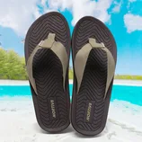 Flip-flops with brown soles and beige straps, labeled \“Nortiv8,\“ set against a tropical beach background.