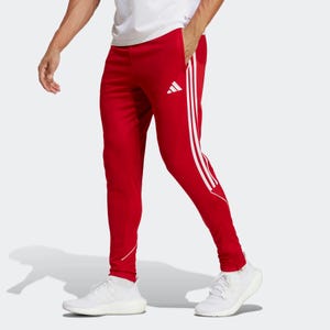 A person wearing red track pants with white stripes and logo, paired with a white t-shirt and white sneakers.