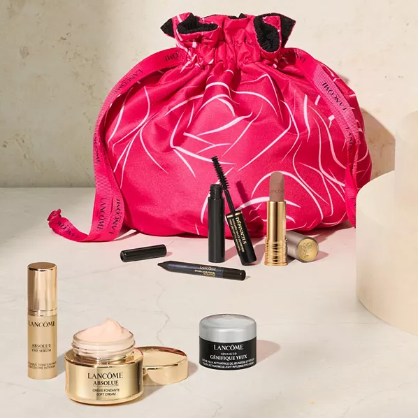 A collection of Lancôme cosmetics including mascara, lipstick, foundation, and skincare creams, displayed with a red drawstring bag.