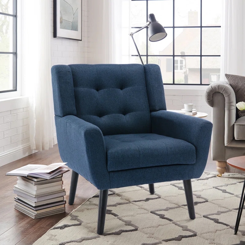 Blue mid-century modern armchair with tufted backrest, positioned on a geometric-patterned rug near a stack of books and a standing lamp in a bright living room.