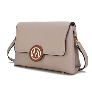 A beige handbag with a flap closure, featuring a circular emblem with an \“M\“ logo, and an adjustable strap.