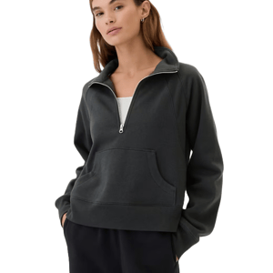 A woman is wearing a relaxed fleece quarter-zip sweatshirt in dark gray, featuring a front pocket with a white shirt underneath.